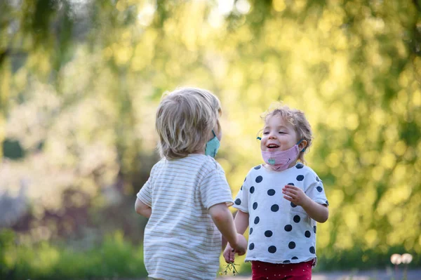 Small children with face masks playing outdoors, coronavirus concept. — Stock Photo, Image
