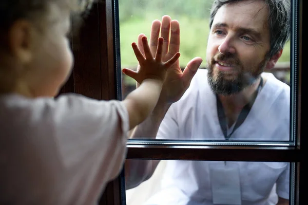 Doctor viniendo a ver a la familia en aislamiento, vidrio de la ventana separándolos . —  Fotos de Stock