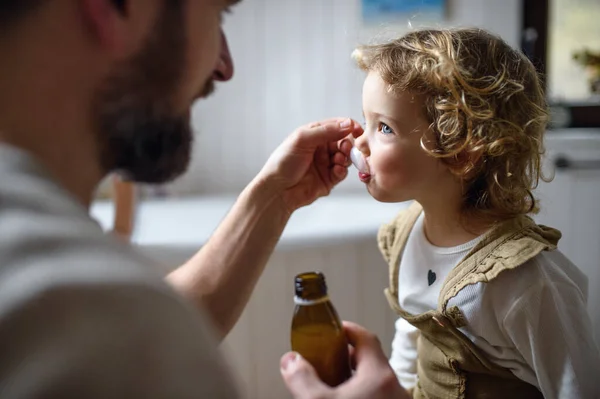 Ayah tak dikenal memberikan sirup pada anak kecil yang sakit di dalam rumah.. — Stok Foto