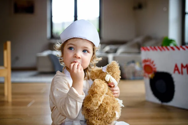 Petite fille tout-petit avec uniforme médecin à l'intérieur à la maison, jouer . — Photo