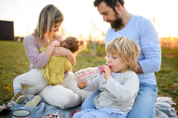Familia con dos niños pequeños haciendo picnic al aire libre en primavera al atardecer . — Foto de Stock