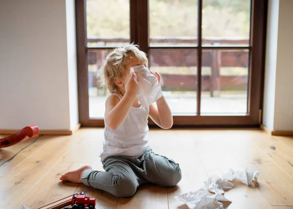 Anak kecil yang sakit dengan dingin di rumah duduk di tanah, bersin. — Stok Foto