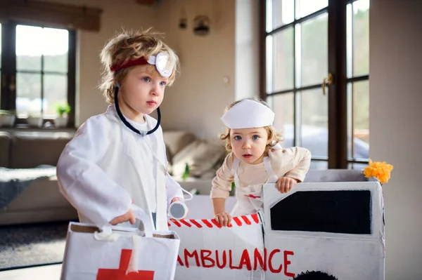 Due bambini piccoli con uniformi da medico in casa, che giocano . — Foto Stock