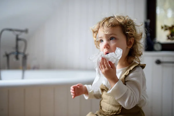 Liten sjuk flicka med kallt hemma sitter på marken, blåser näsa. — Stockfoto