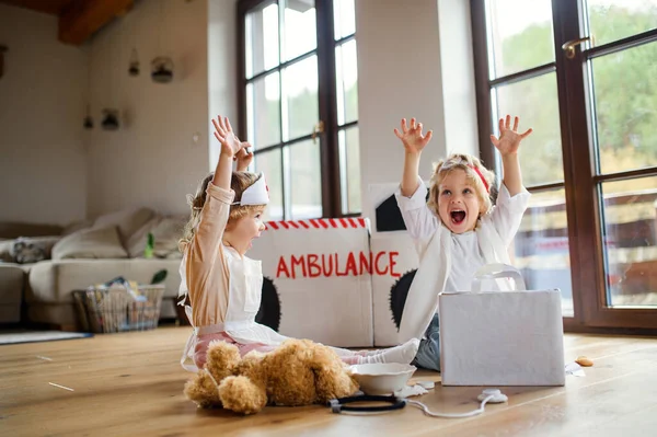 Dos niños pequeños con uniformes médicos en casa, divirtiéndose al jugar . —  Fotos de Stock