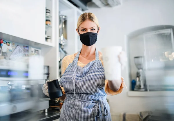 Coffee shop woman owner working with face mask, open after lockdown quarantine.