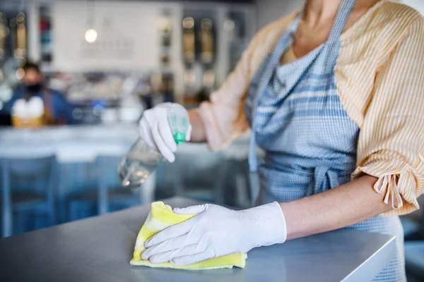 Femme méconnaissable travaillant avec des gants dans un café, désinfectant les tables . — Photo
