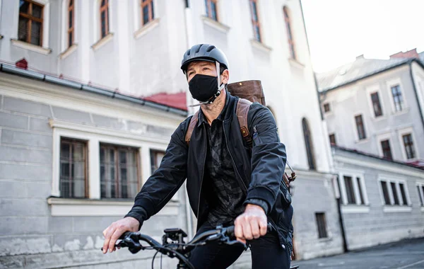 얼굴에 마스크를 쓰고 자전거를 타고 마을로 오는 배달 직원. — 스톡 사진