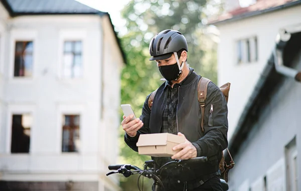 Entrega mensajero hombre con máscara facial y bicicleta usando smartphone en la ciudad . — Foto de Stock