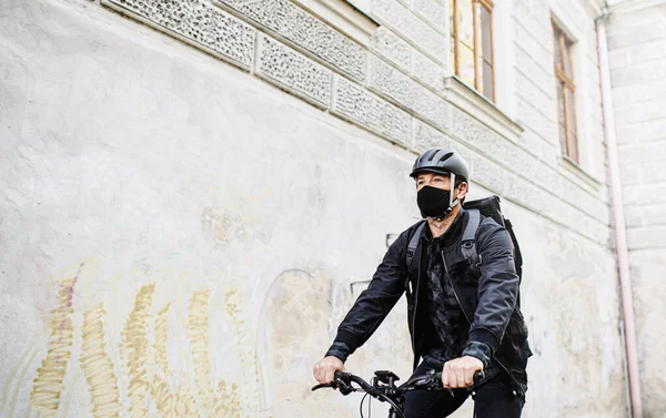 Entrega mensajero hombre con máscara facial y ciclismo en bicicleta en la ciudad . —  Fotos de Stock