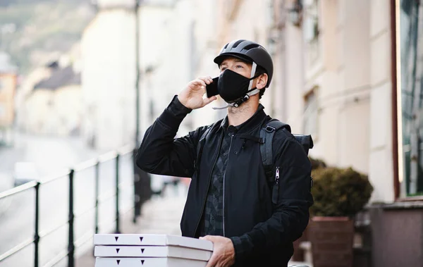 Курьер с маской для лица и смартфоном доставляет пиццу в город . — стоковое фото