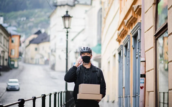 Курьер с маской для лица и смартфоном доставляет посылку в город . — стоковое фото