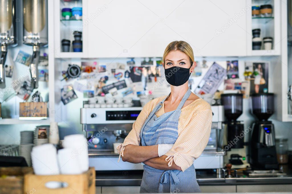 Woman owner with face mask in coffee shop, lockdown and back to normal concept.