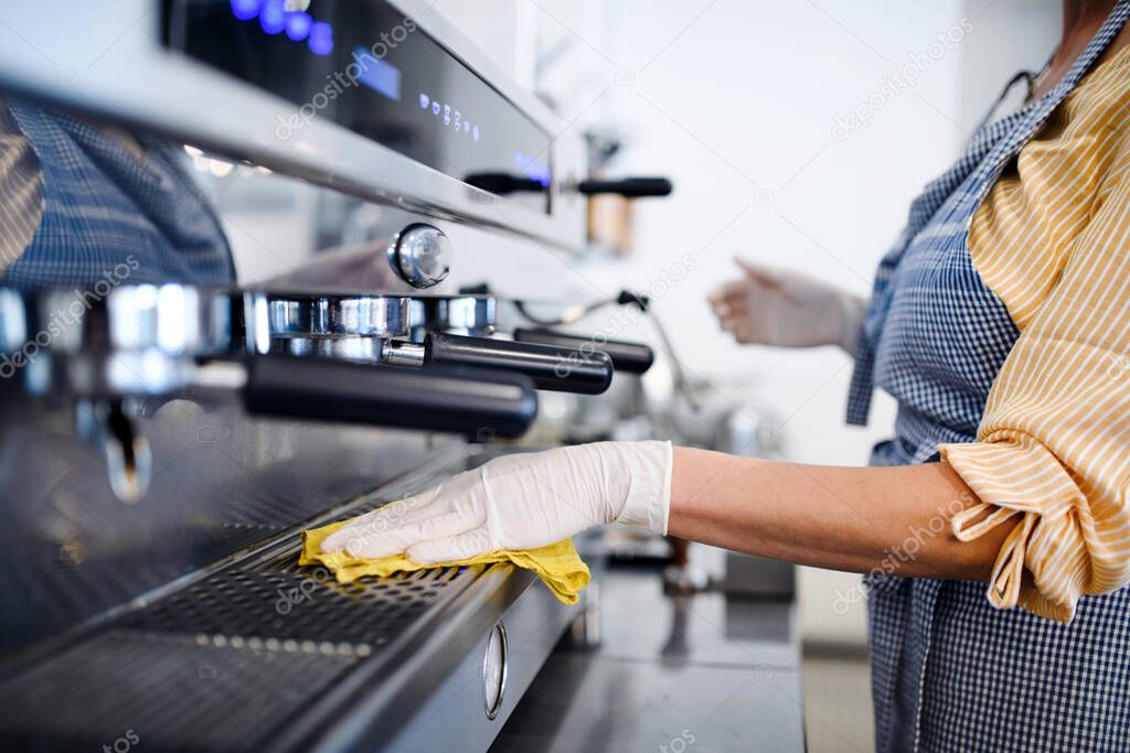 Coffee shop woman owner working with gloves , disinfecting machine.