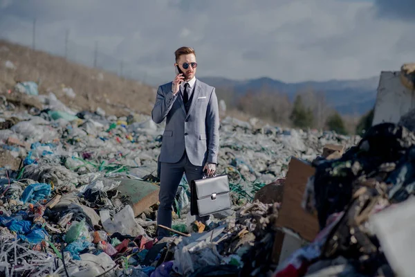 Uomo d'affari con smartphone in discarica, consumismo contro concetto di inquinamento . — Foto Stock