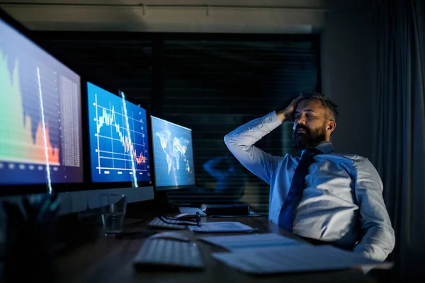 Empresário frustrado com computador sentado à secretária, a trabalhar até tarde. Conceito de crise financeira . — Fotografia de Stock