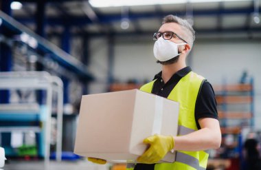 Koruyucu maskeli bir işçi endüstriyel fabrikada ya da depoda çalışıyor..