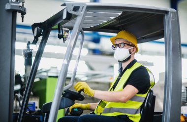 Koruyucu maskeli forklift şoförü endüstriyel fabrikada ya da depoda çalışıyor..