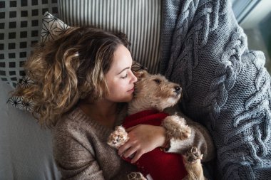 Evcil bir köpekle evdeki kanepede dinlenen genç bir kadın manzarası..