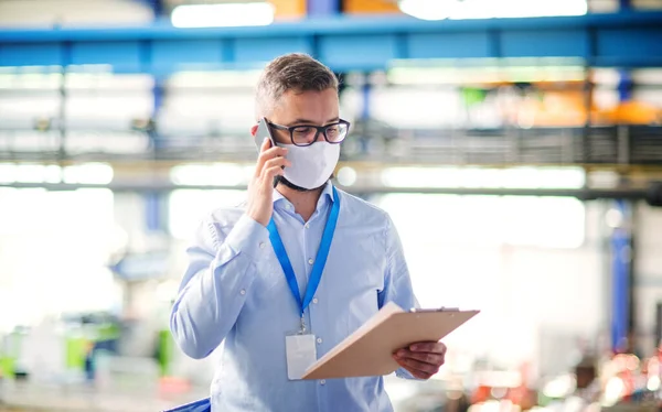 Técnico o ingeniero con máscara protectora y teléfono trabajando en fábrica industrial . — Foto de Stock