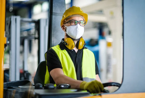 Koruyucu maskeli forklift şoförü endüstriyel fabrikada ya da depoda çalışıyor..