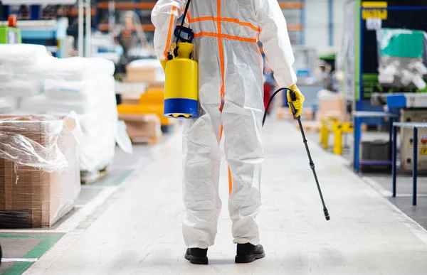 Arbeiter mit Schutzmaske und Anzug desinfiziert Industriefabrik mit Spritzpistole. — Stockfoto