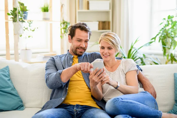 Szczęśliwa para w miłości siedzi w domu, za pomocą smartfona. — Zdjęcie stockowe
