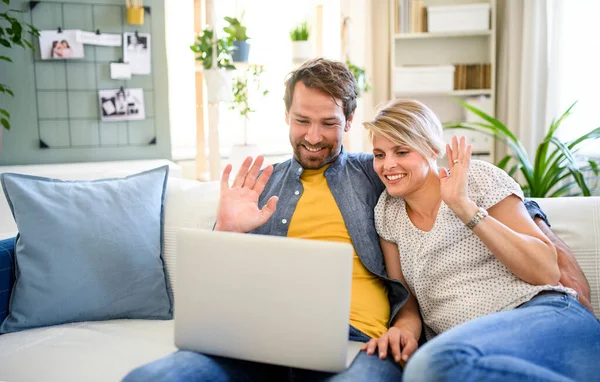 Szczęśliwa para mając wideo rozmowy na laptopie w domu, machając. — Zdjęcie stockowe