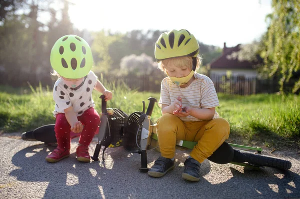 Μικρά παιδιά με μάσκες προσώπου παίζουν σε εξωτερικούς χώρους με ποδήλατο, έννοια coronavirus. — Φωτογραφία Αρχείου