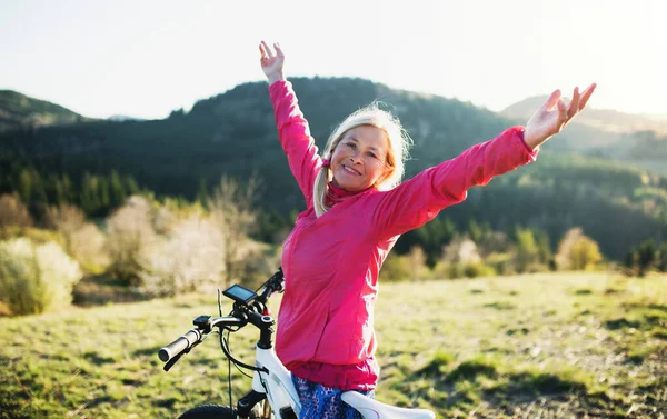 Ενεργός ηλικιωμένη γυναίκα με e-bike σε εξωτερικούς χώρους στη φύση, τα χέρια τεντωμένα. — Φωτογραφία Αρχείου