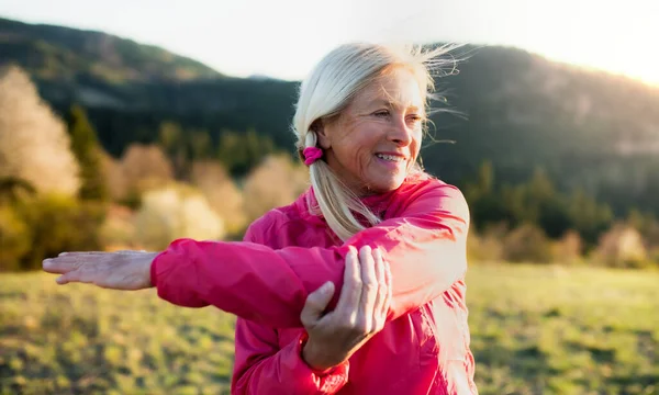 Atractiva mujer mayor haciendo ejercicio al aire libre en la naturaleza, estiramiento . — Foto de Stock