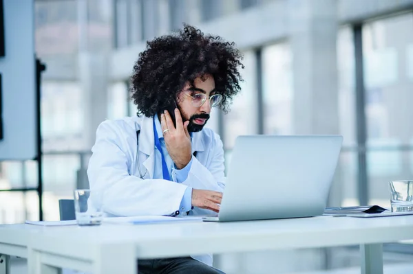 Portrait du médecin assis à l'hôpital, à l'aide d'un ordinateur portable et d'un smartphone . — Photo