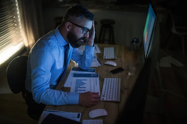 Frustrerad affärsman med datorn sitter vid skrivbordet, arbetar sent. Begreppet finansiell kris. — Stockfoto