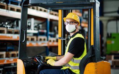Koruyucu maskeli forklift şoförü endüstriyel fabrikada ya da depoda çalışıyor..