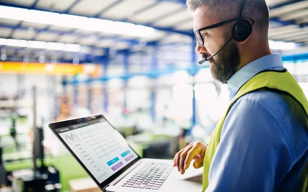 Sidovy av tekniker eller ingenjör med headset och bärbar dator stående i industriell fabrik. — Stockfoto