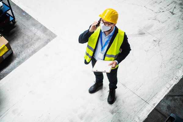 Technician or engineer with protective mask and helmet working in industrial factory.