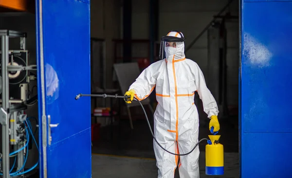 Travailleur homme avec masque de protection et costume désinfectant usine industrielle avec pistolet pulvérisateur . — Photo