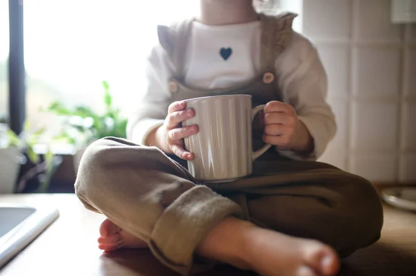 Middel van peuter meisje zit op het aanrecht binnen thuis, holding cup. — Stockfoto