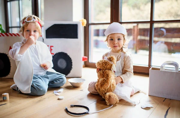 Dos niños pequeños con uniformes médicos en casa, jugando . — Foto de Stock