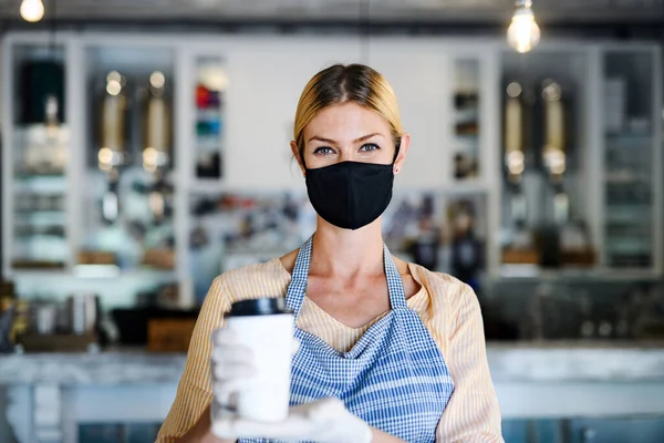 Woman owner with face mask in coffee shop, lockdown and back to normal concept.
