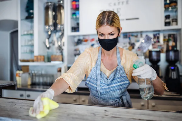 Владелец кофейни работает в маске и перчатках, дезинфицирует прилавок . — стоковое фото