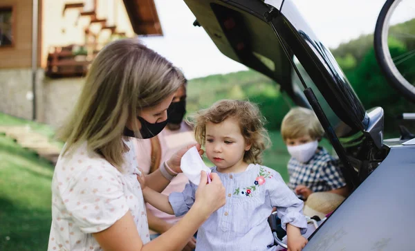 Οικογένεια με δύο μικρά παιδιά που φορτώνουν αυτοκίνητο για ταξίδι στην εξοχή, φορώντας μάσκες προσώπου. — Φωτογραφία Αρχείου