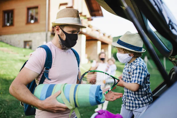 Família com duas crianças pequenas carregando carro para viagem no campo, usando máscaras faciais . — Fotografia de Stock