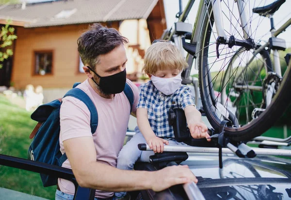 Apa kisfiúval bicikliket tesz az autó tetejére, arcmaszkot visel.. — Stock Fotó