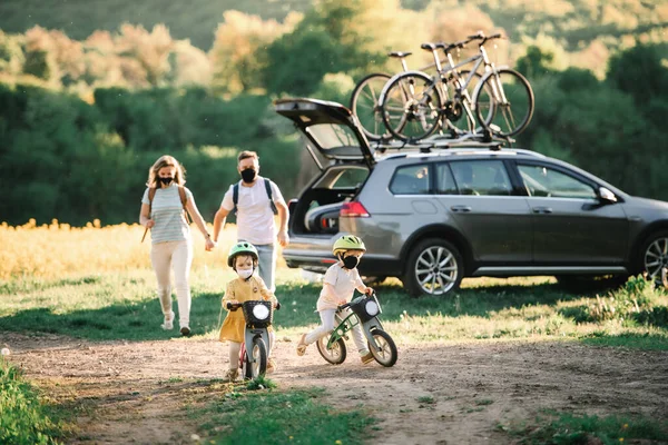 Família com duas crianças pequenas e máscaras faciais em viagem de bicicleta no campo . — Fotografia de Stock