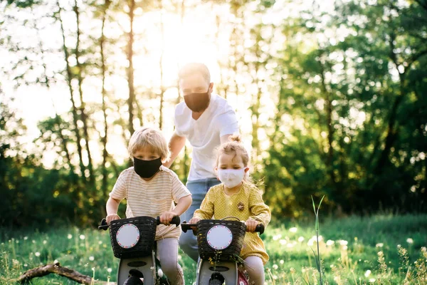 Père avec deux jeunes enfants et masques pour le visage en randonnée à vélo dans la nature . — Photo