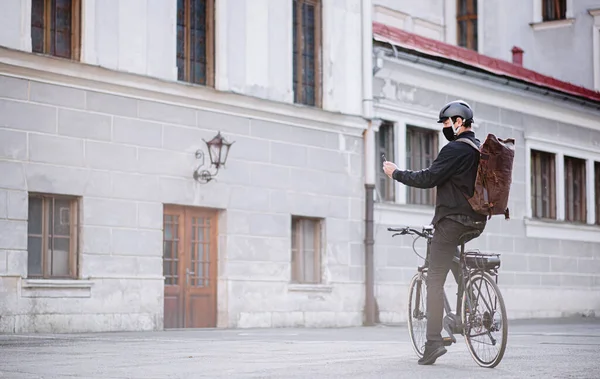 Entrega mensajero hombre en bicicleta con máscara facial y entrega de teléfonos inteligentes en la ciudad . — Foto de Stock