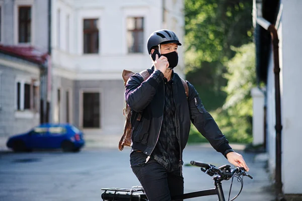 Kurýr doručovatel s obličejovou maskou a jízdním kolem pomocí smartphonu ve městě. — Stock fotografie