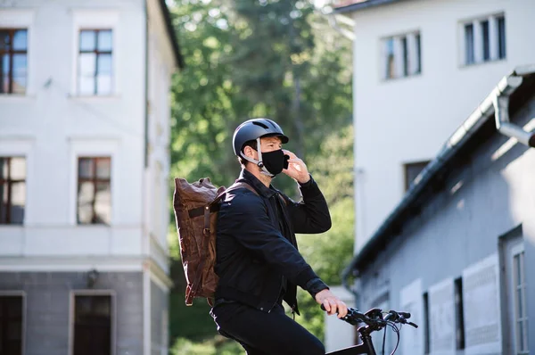 Entrega mensajero hombre en bicicleta con máscara facial y entrega de teléfonos inteligentes en la ciudad . —  Fotos de Stock