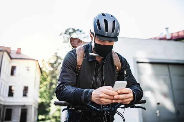 Entrega mensajero hombre con máscara facial y bicicleta usando smartphone en la ciudad . — Foto de Stock